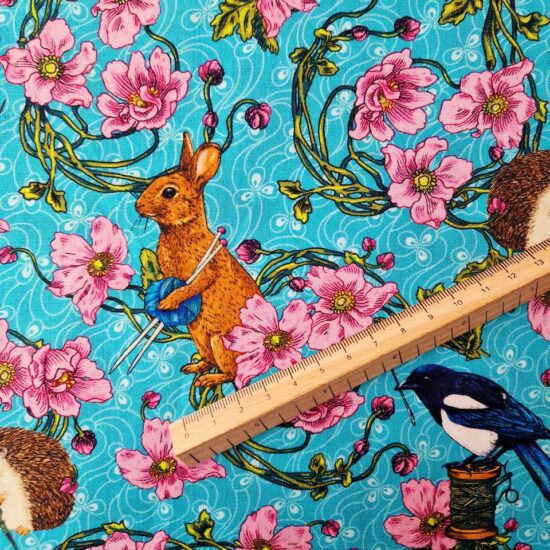 Coton imprimé sur le fond bleu turquoise des fleurs roses, les tiges vertes qui encerclent un lapin roux avec sa pelote de laine aiguille à tricoter sous le bras