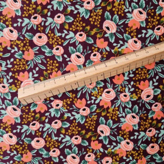 tissu imprimé fleuri comme un semis de fleurs délicat et raffiné boules de fleurs rose corail sur un fond prune feuillage vert et ocre